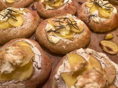 Mini focaccia cu cartofi, brânză de capră și cremă de brânză se află pe o foaie de hârtie de copt. Toate focaccias sunt presărate cu fulgi de drojdie și rozmarin.