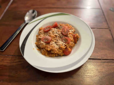 Ein Teller mit Tomatenrisotto, dekoriert mit würzigen Hefeflocken, steht auf einem Holztisch, daneben ein Löffel.