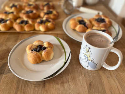 On a plate is a yeast flower decorated with vanilla pudding and blueberries, in the background a baking tray with more yeast pieces